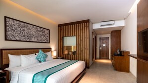 A modern hotel room with a large bed, a wooden headboard, a wall-mounted artwork, a bathroom mirror, and a TV. - Anja Jimbaran (Jimbaran)