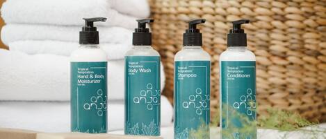 Three bottles of Tropical Temptation Body Wash, Hand & Body Moisturizer, and Shampoo, each with a 250 ml capacity, placed on a white surface with a woven basket and folded towels in the background.