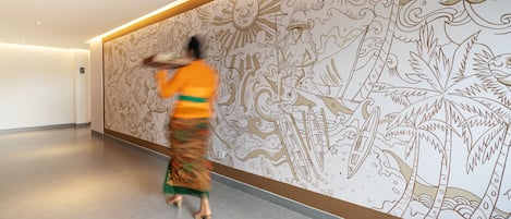 Un pasillo con un gran mural que presenta diseños tradicionales y una mujer caminando.