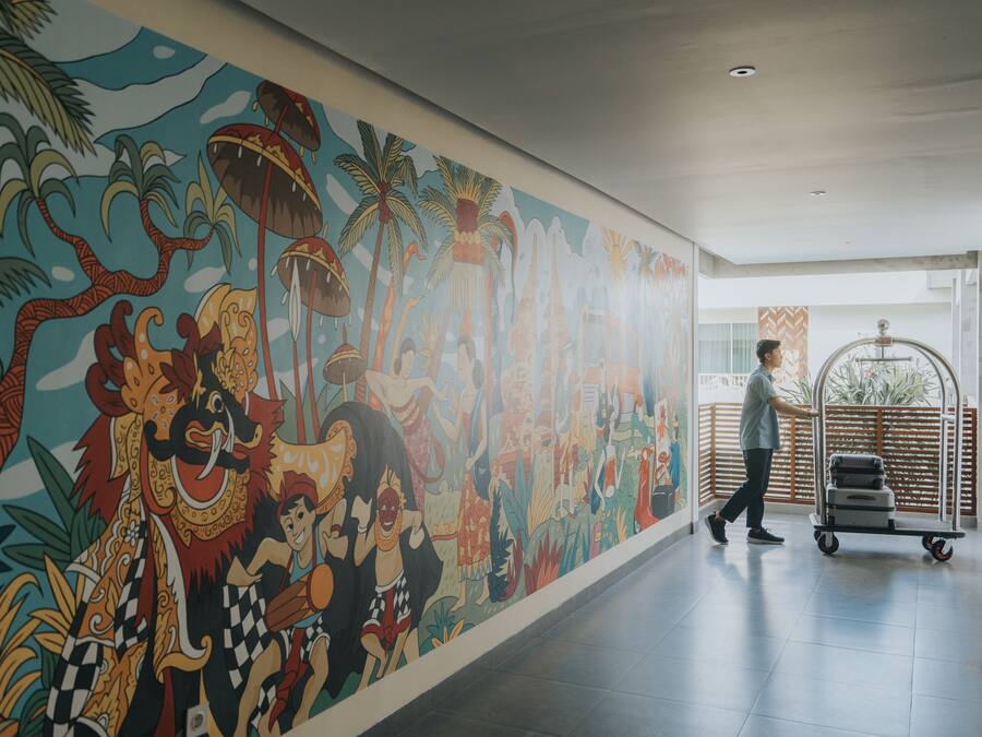 Un mural con motivos tropicales y culturales, un carrito de equipaje y una persona caminando en un moderno vestíbulo de hotel.