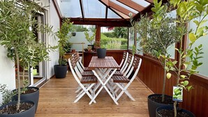 Eine Holzdielen-Terrasse mit Tisch und Stühlen, umgeben von Blumentöpfen.
