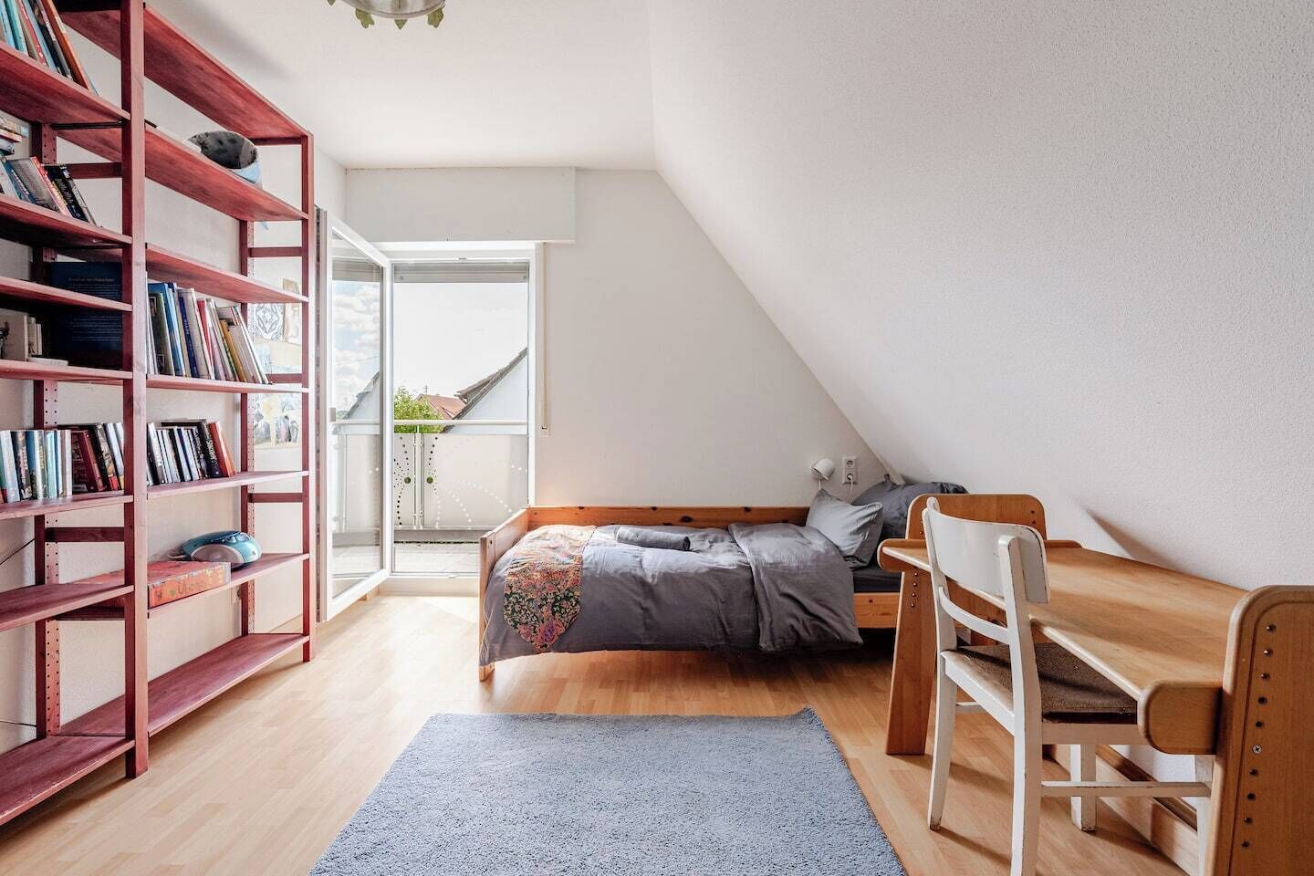 Un dormitorio pequeño y acogedor con cama altillo, un escritorio de madera y una estantería.