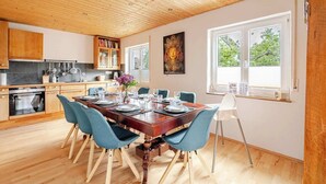 Eine moderne Küche mit Holzschränken, einem Esstisch für sechs Personen und einem großen Fenster mit hellem Tageslicht.