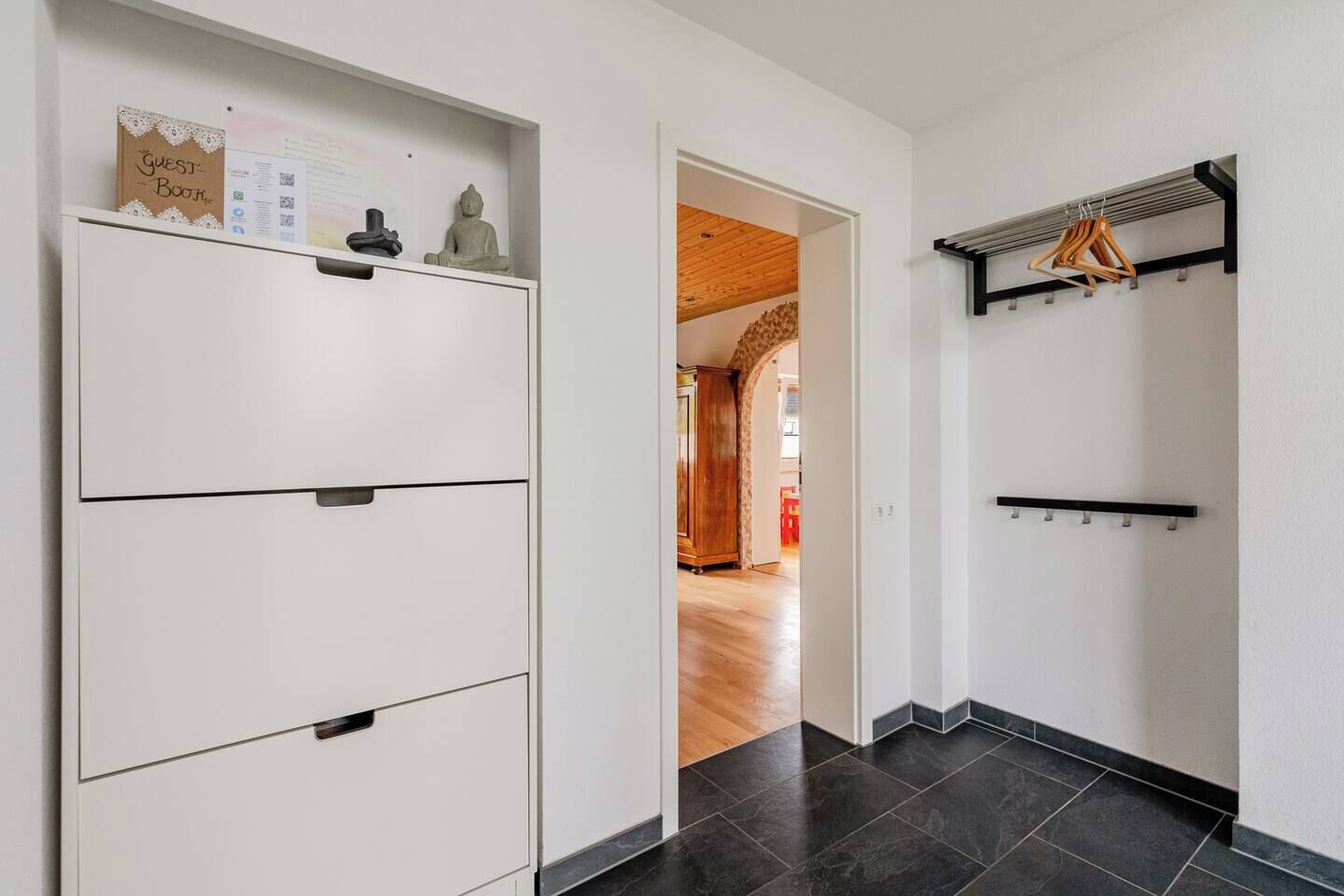 Ein Flur mit einem weißen Schrank, einer Holztür zu einem anderen Zimmer und einem schwarzen, an der Wand befestigten Kleiderständer.