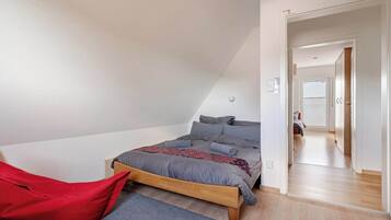 Una camera da letto con soffitto spiovente, un letto con biancheria grigia, una sedia rossa e un pavimento in legno.