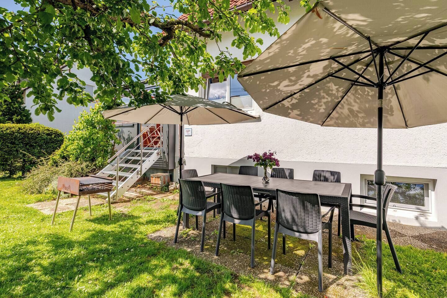 An outdoor patio with a table and chairs, two large umbrellas, and a staircase leading to a building.