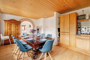 A dining area with a wooden table set for six, blue chairs, and a kitchen with wooden cabinets and appliances.