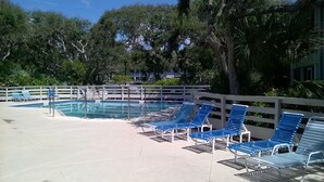 A swimming pool with blue lounge chairs and a white fence.
