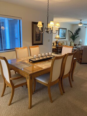 A dining area with a glass-top table, wooden chairs, a chandelier, and a framed picture on the wall.