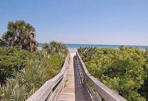 A wooden boardwalk leading to a beach with dense greenery on both sides.