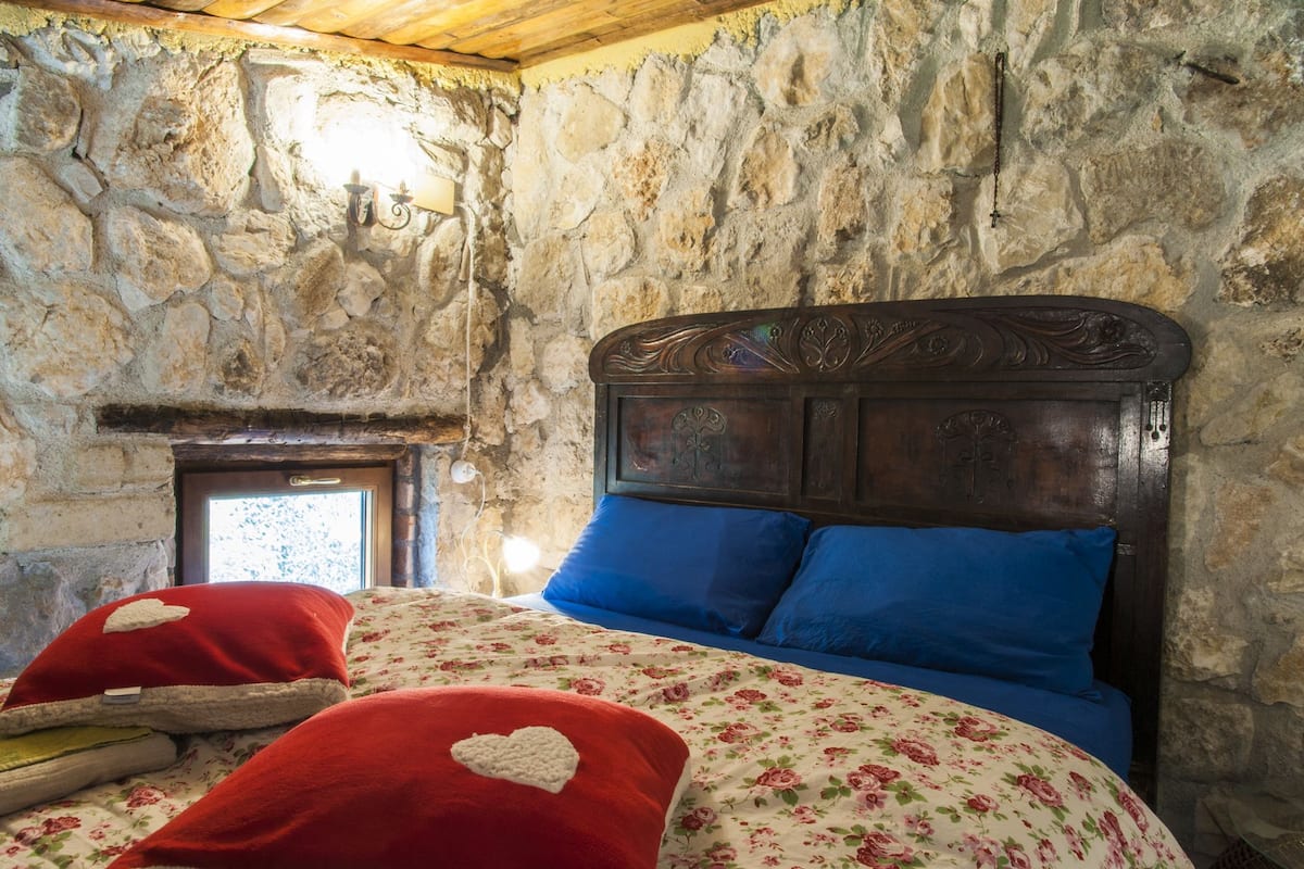 Un dormitorio con pared de piedra, estructura de cama de madera y colcha con estampado floral.
