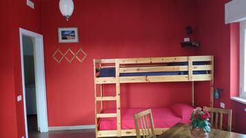 Una habitación con una cama individual superpuesta, una mesa de madera con sillas, un florero con flores y una ventana.