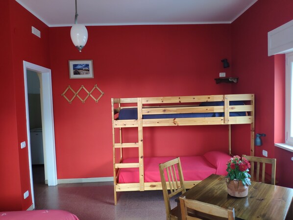 A room with a bunk bed, a wooden table with chairs, a vase with flowers, and a window. - B&B De Angelis (Ginosa)