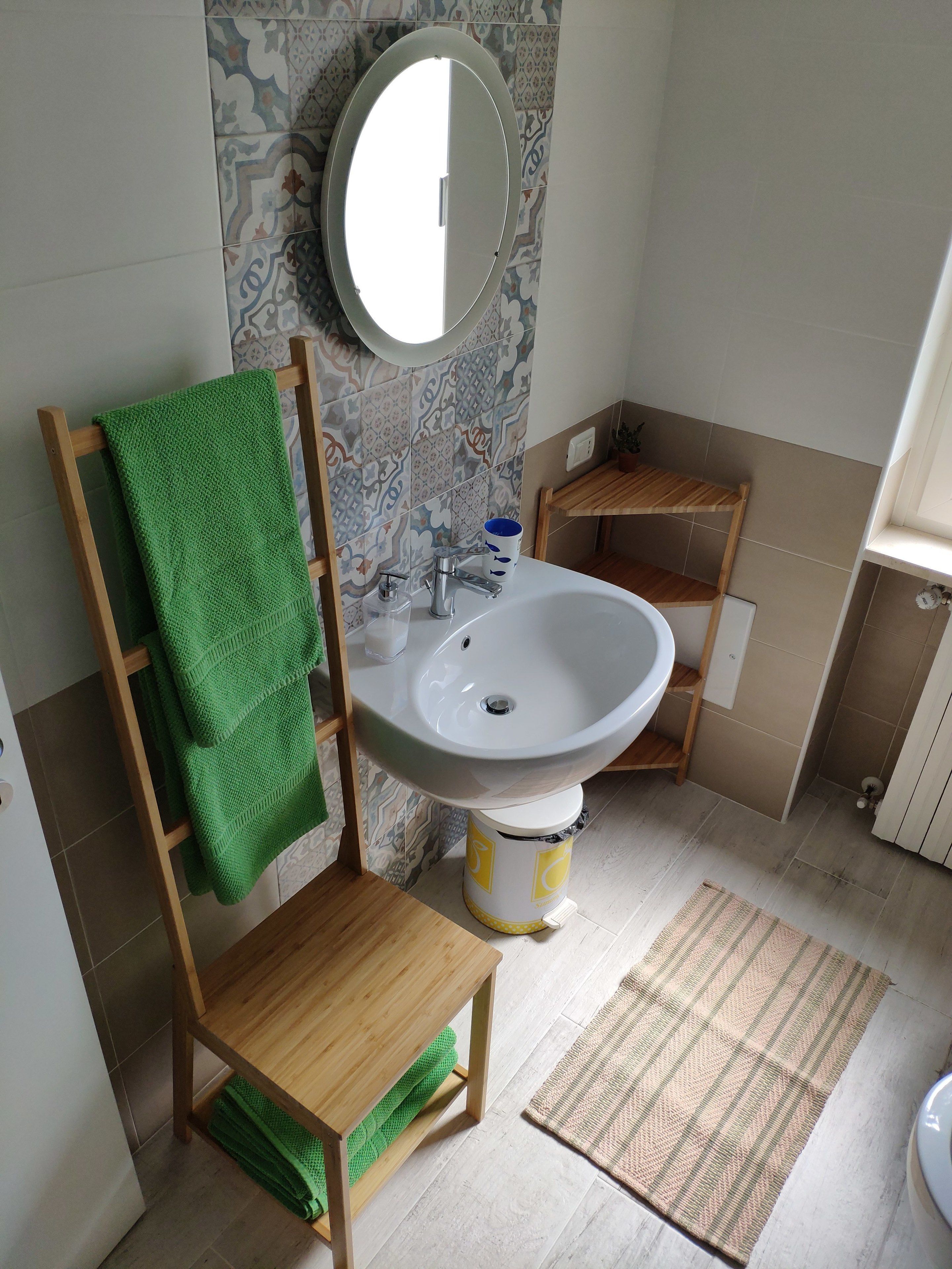 Un baño con una silla de madera, una toalla verde, un lavamanos, un espejo y baldosas estampadas.