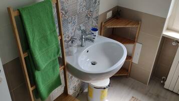 Un baño con una silla de madera, una toalla verde, un lavamanos, un espejo y baldosas estampadas.