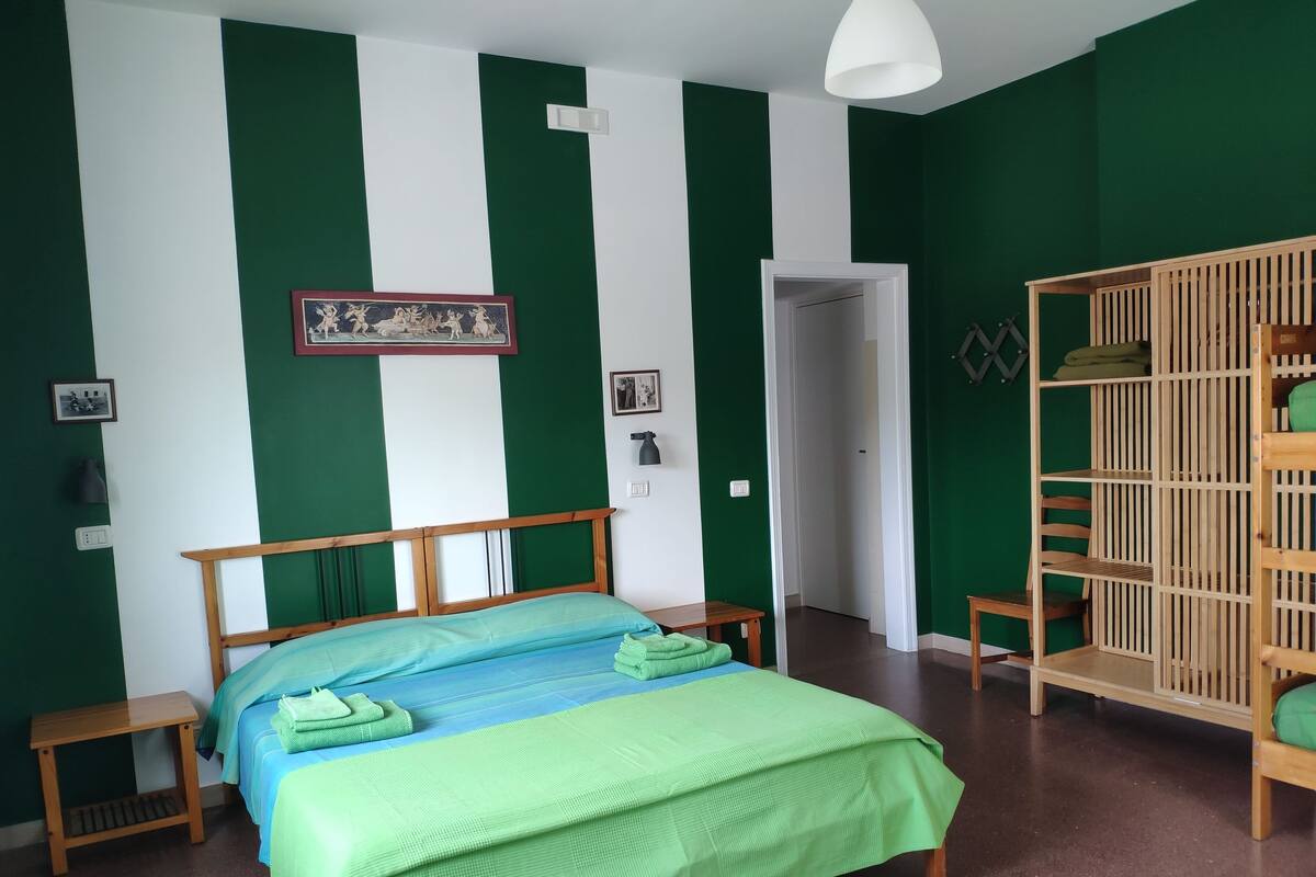 A room with a bed, a wooden nightstand, a wardrobe, and a door leading to another room.