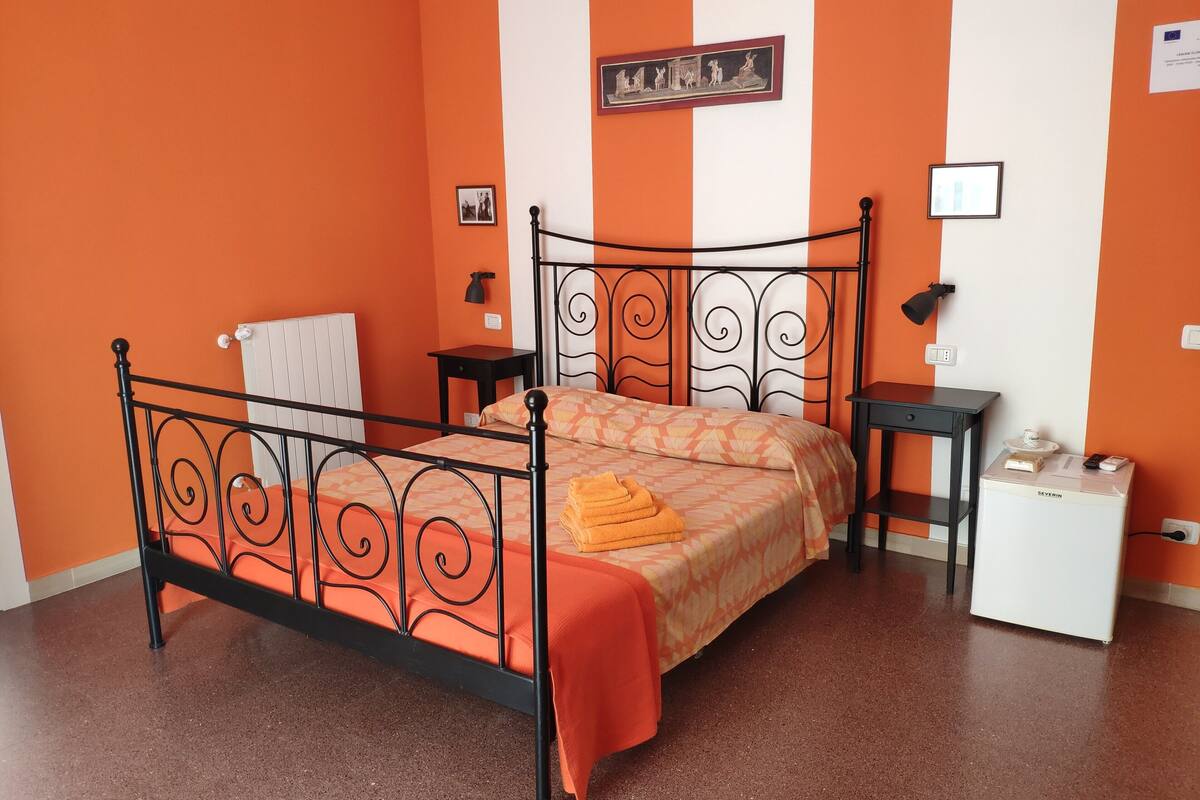 A bed with a metal frame, a bedside table, a nightstand, a radiator, and a wall-mounted picture.