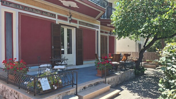 A building with a red facade, a balcony with outdoor seating, and a tree providing shade. - B&B De Angelis (Ginosa)