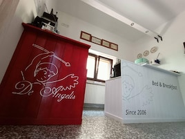 Una habitación con un armario rojo que presenta un diseño de ángel de dibujos animados y el texto "De Angelis". Hay un armario blanco con la etiqueta "Bed & Breakfast" y "Desde 2006".