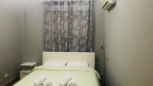 A hotel room with a bed, a nightstand, a towel, a curtain, and an air conditioning unit. - Smart Location (Athens)