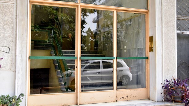 A building entrance with large glass doors, a visible staircase, and a parked car inside. - Smart Location (Athens)