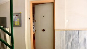 A room with a closed door, a radiator, a wall-mounted electrical box, and a marble-patterned wall. - Smart Location (Athens)