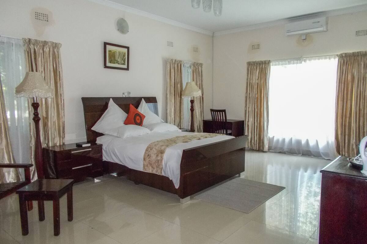 A hotel room with a large bed, a desk, a chair, and a window with curtains.