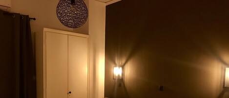 Quarto de hotel com cama bem arrumada, cabeceira de madeira, luminária na parede e porta fechada.