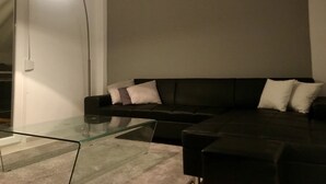 A modern living room with a glass coffee table, a black leather sofa with white cushions, and a floor lamp. - Renovated minimal aptm next to metro (Athens)