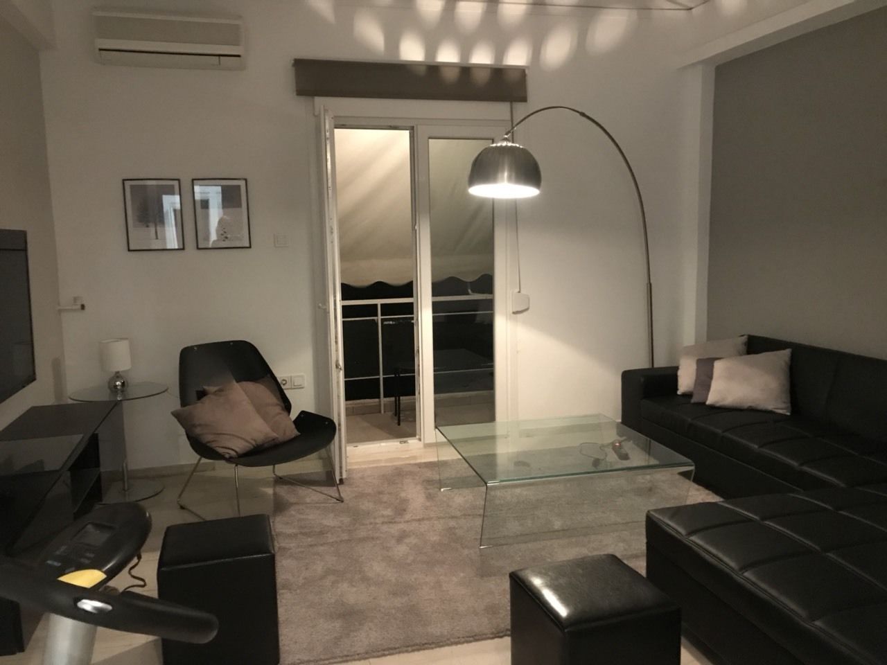 A modern living room with a glass coffee table, black sofas, a black chair, a TV, and a large floor lamp.