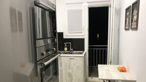 A compact kitchen with a built-in oven, a sink, and a small table with towels. - Renovated minimal aptm next to metro (Athens)