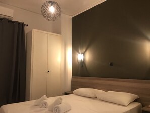 Quarto de hotel com cama, guarda-roupa, mesa de cabeceira e luminária fixada na parede.
