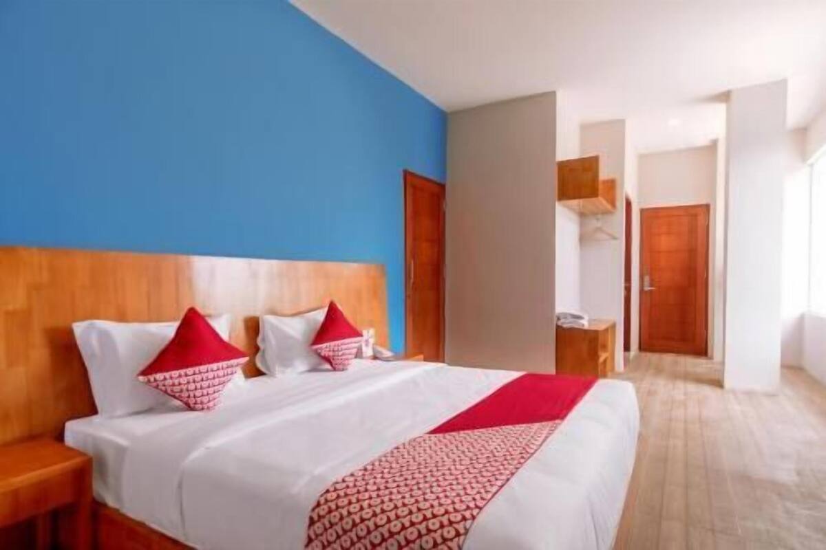 Hotellihuone, jossa on sänky, puinen pääty ja punavalkoinen kuviollinen päiväpeite.
