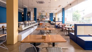 A modern restaurant with wooden tables and chairs, a kitchen area, and large windows offering a view of the street. - Townhouse Oak Medan near Universitas Sumatera Utara formerly Raz Residence (Medan)