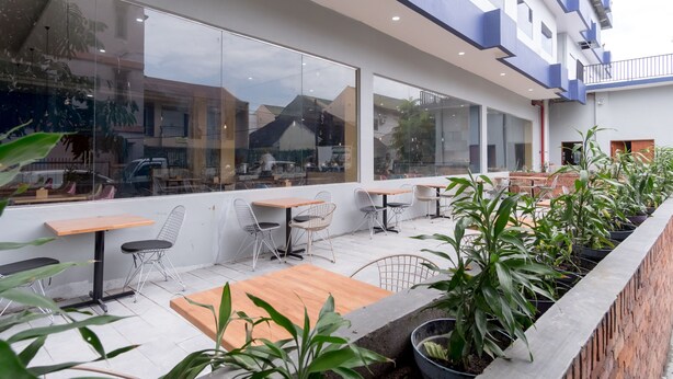 A modern outdoor seating area with tables and chairs, large windows, and potted plants. - Townhouse Oak Medan near Universitas Sumatera Utara formerly Raz Residence (Medan)