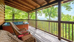Une terrasse en bois avec un jacuzzi, des fauteuils en osier et une vue sur les arbres et les montagnes.