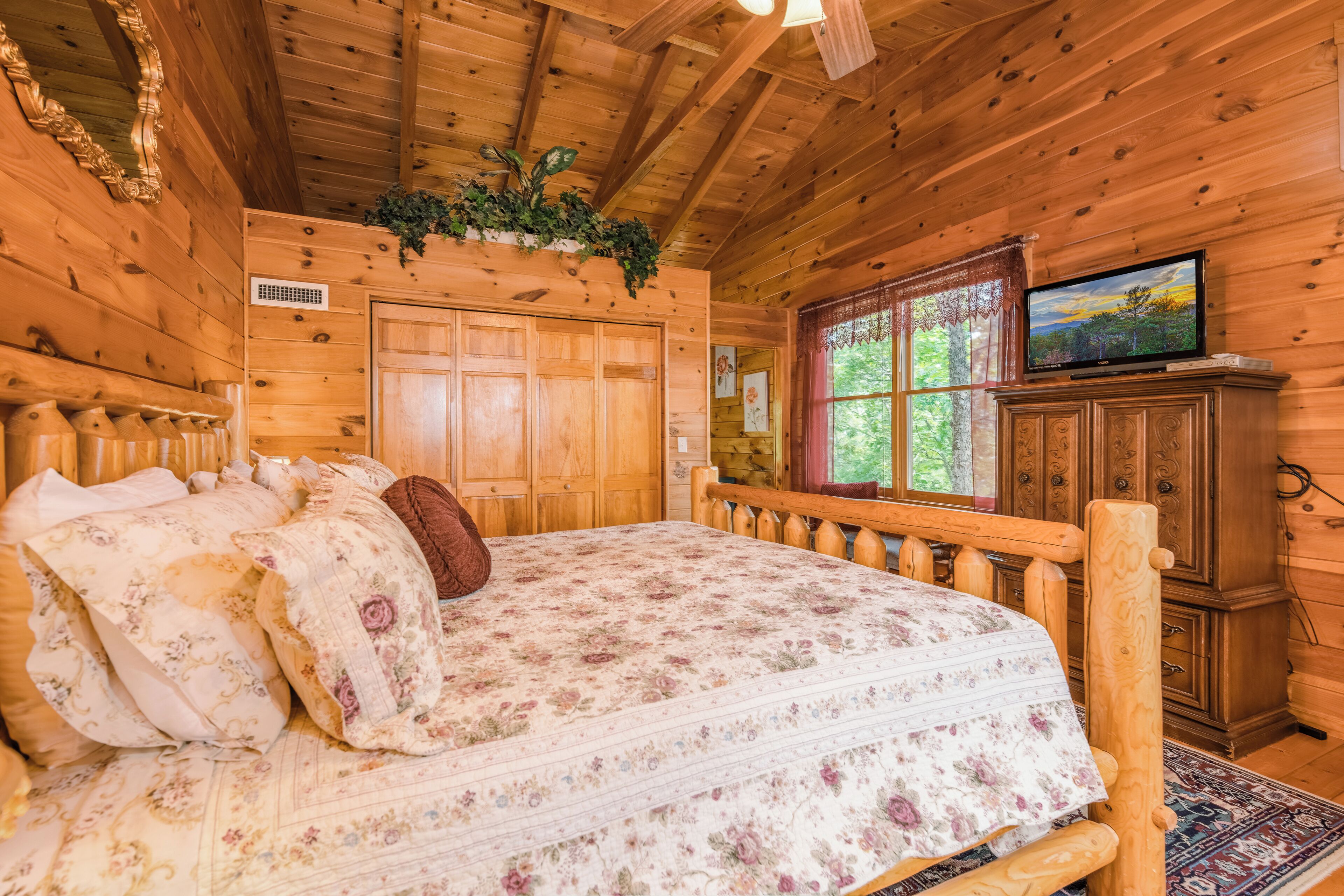 A wooden cabin bedroom with a bed, a television, and a window with curtains.