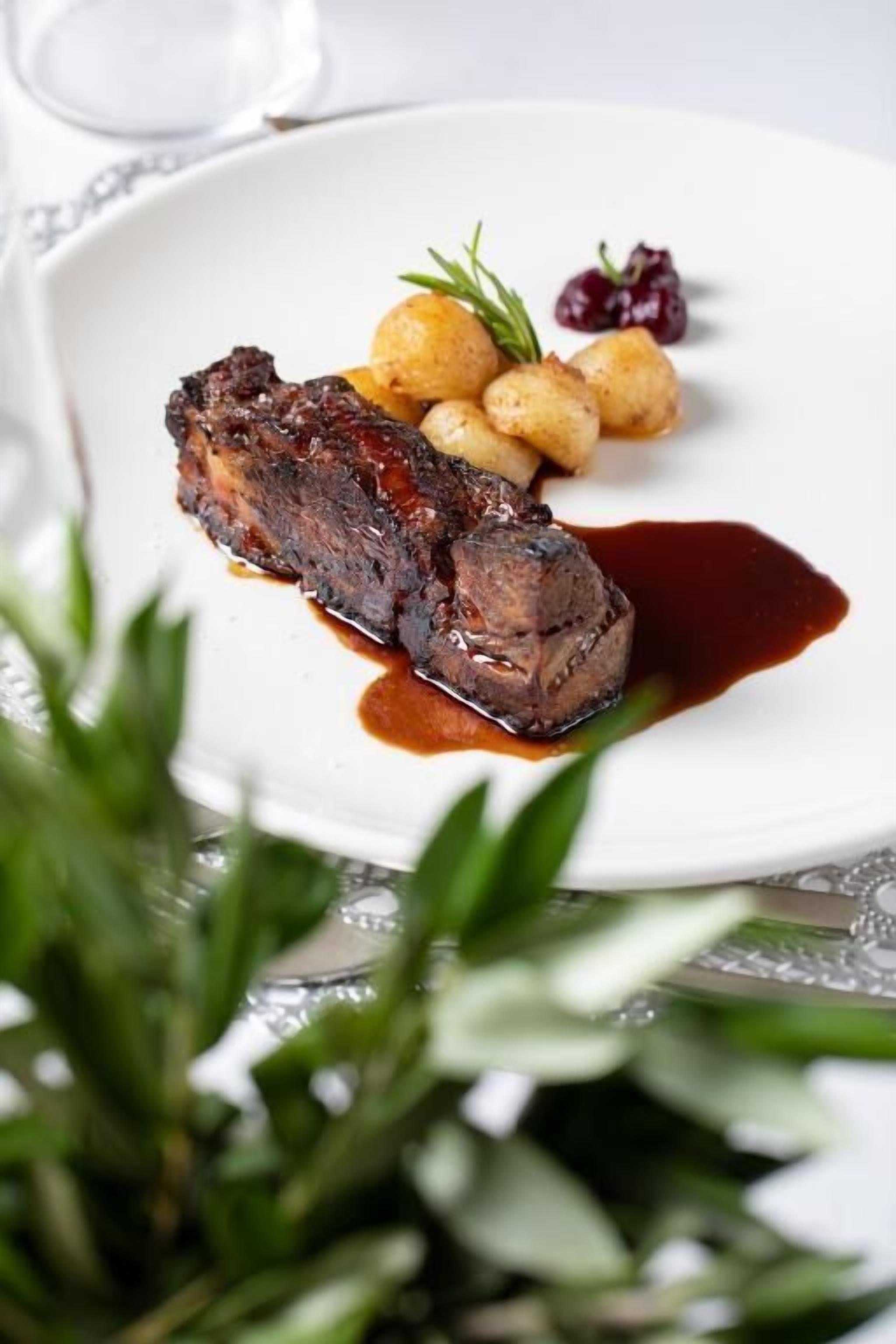 A plate with a piece of meat, potatoes, and a small garnish.