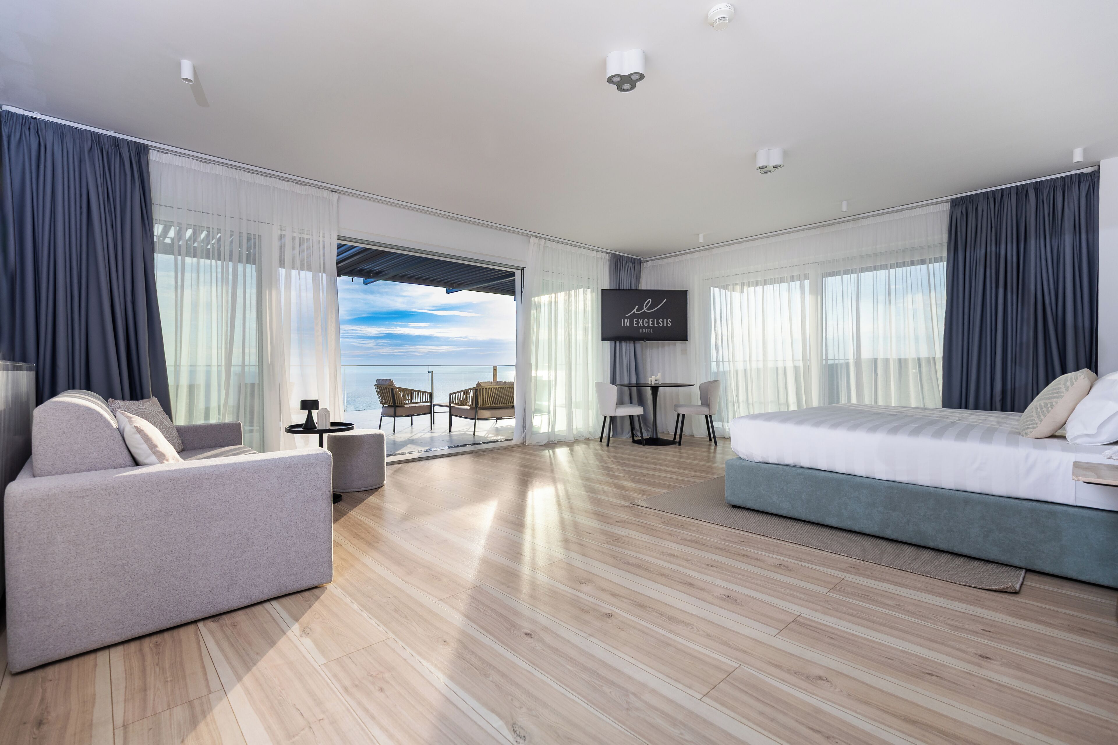A modern hotel room with a large bed, a sofa, a small table, and a TV.