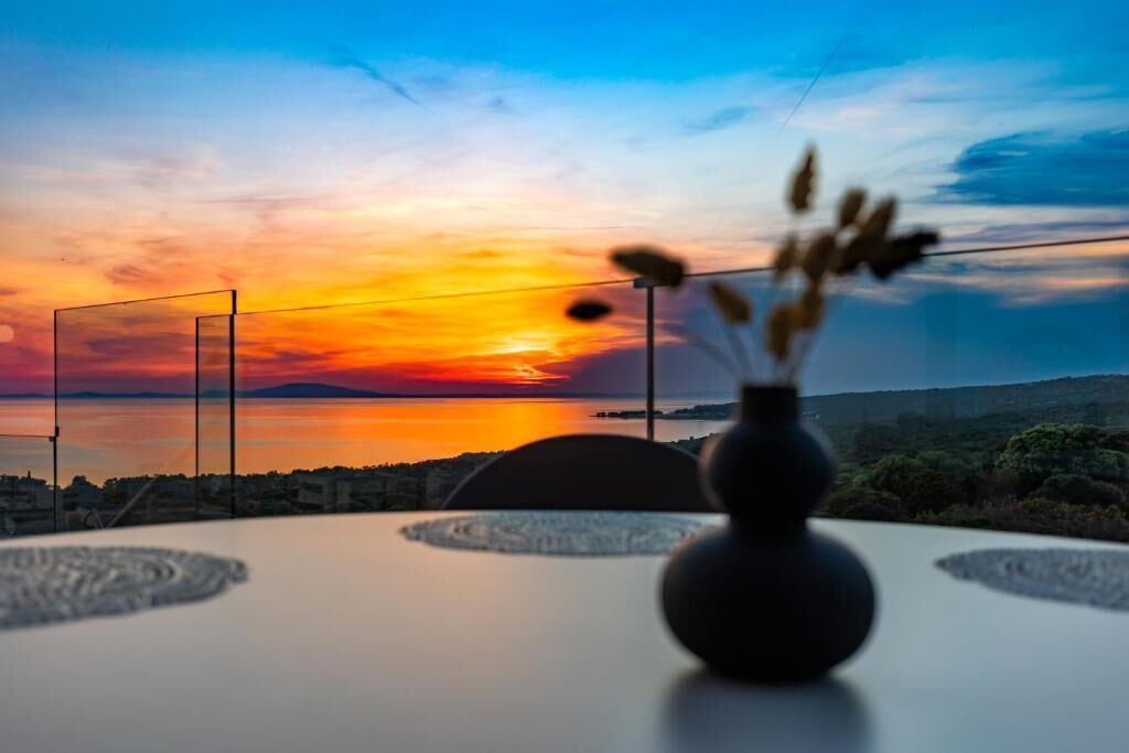 Una mesa con un florero de plantas secas, una silla y una vista del atardecer sobre el agua.