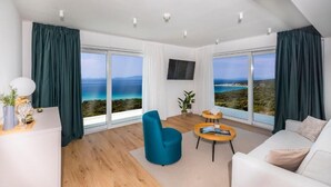 A modern living room with a large window offering a scenic view of the coastline. - Hotel In Excelsis (Novalja)