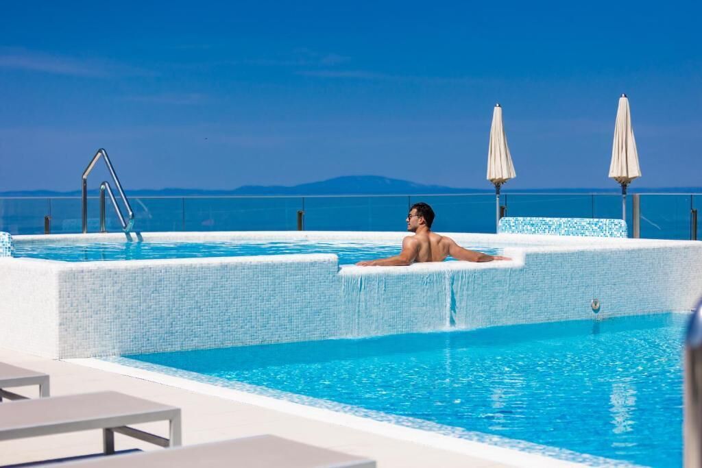 A man relaxing in a pool with a view of the sea and mountains.