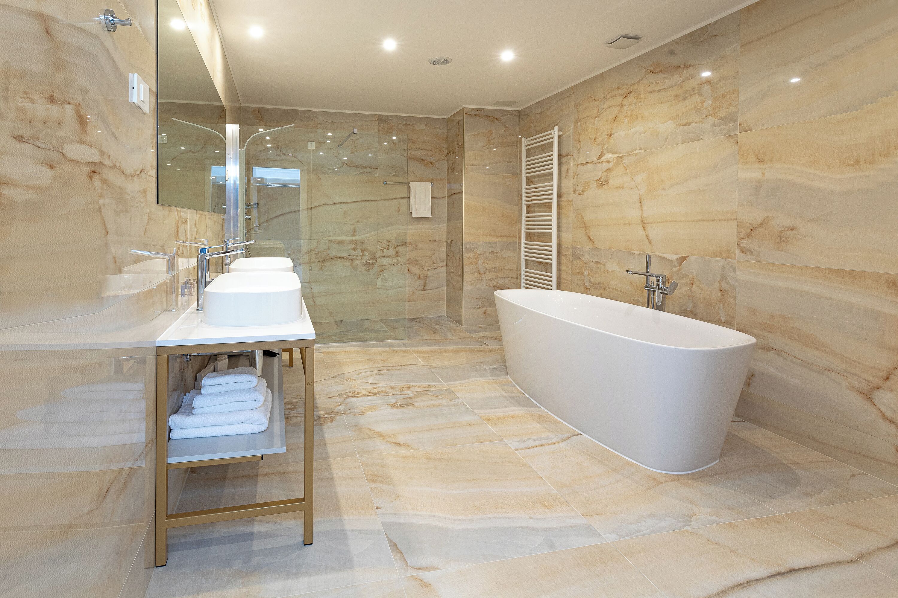 A modern bathroom with marble walls, a freestanding bathtub, and a vanity with a towel rack.