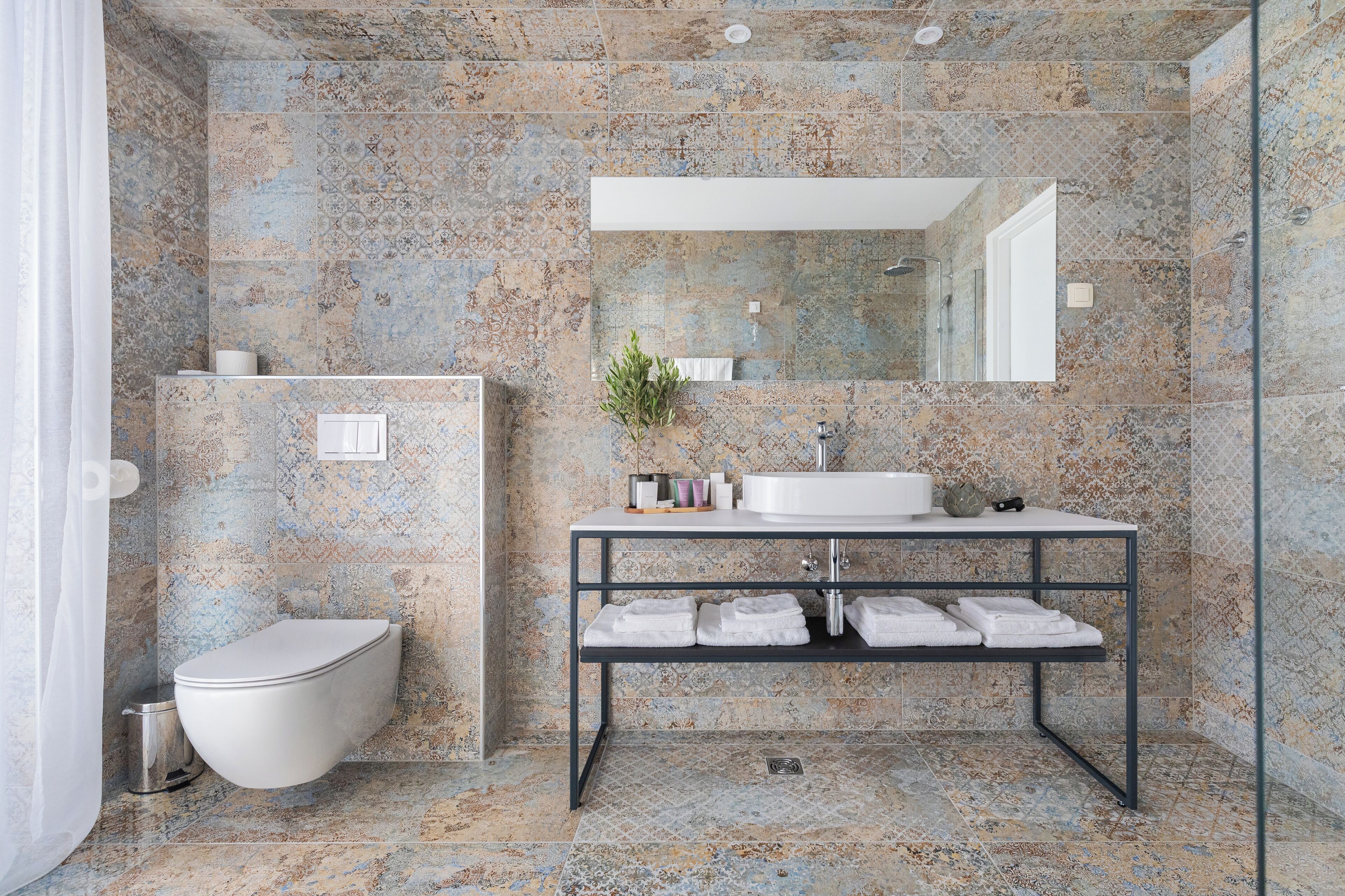 A bathroom with a stone wall, a white toilet, a sink with a mirror, and a shelf with towels.