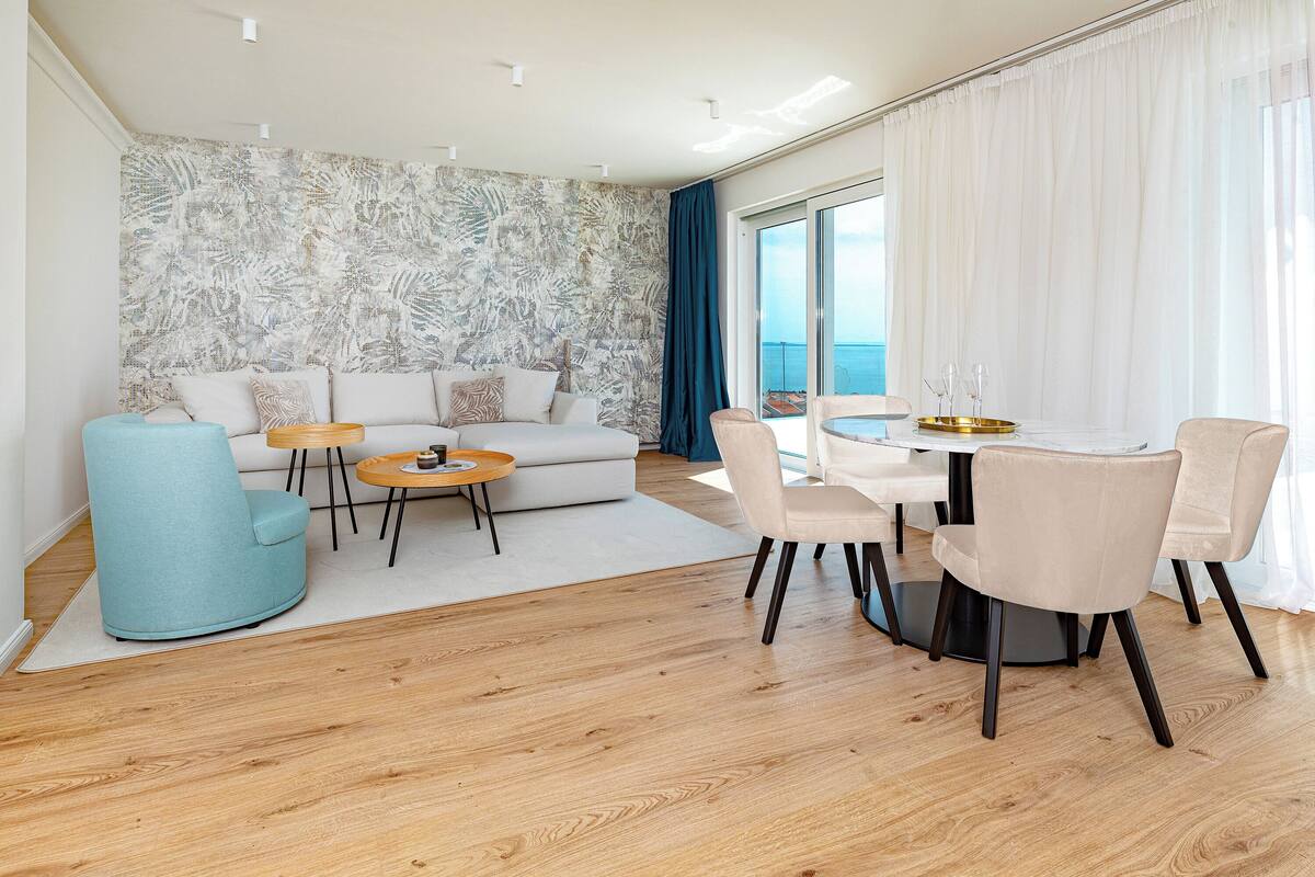 A modern living room with a sofa, armchairs, a coffee table, and a dining area with a table and chairs.