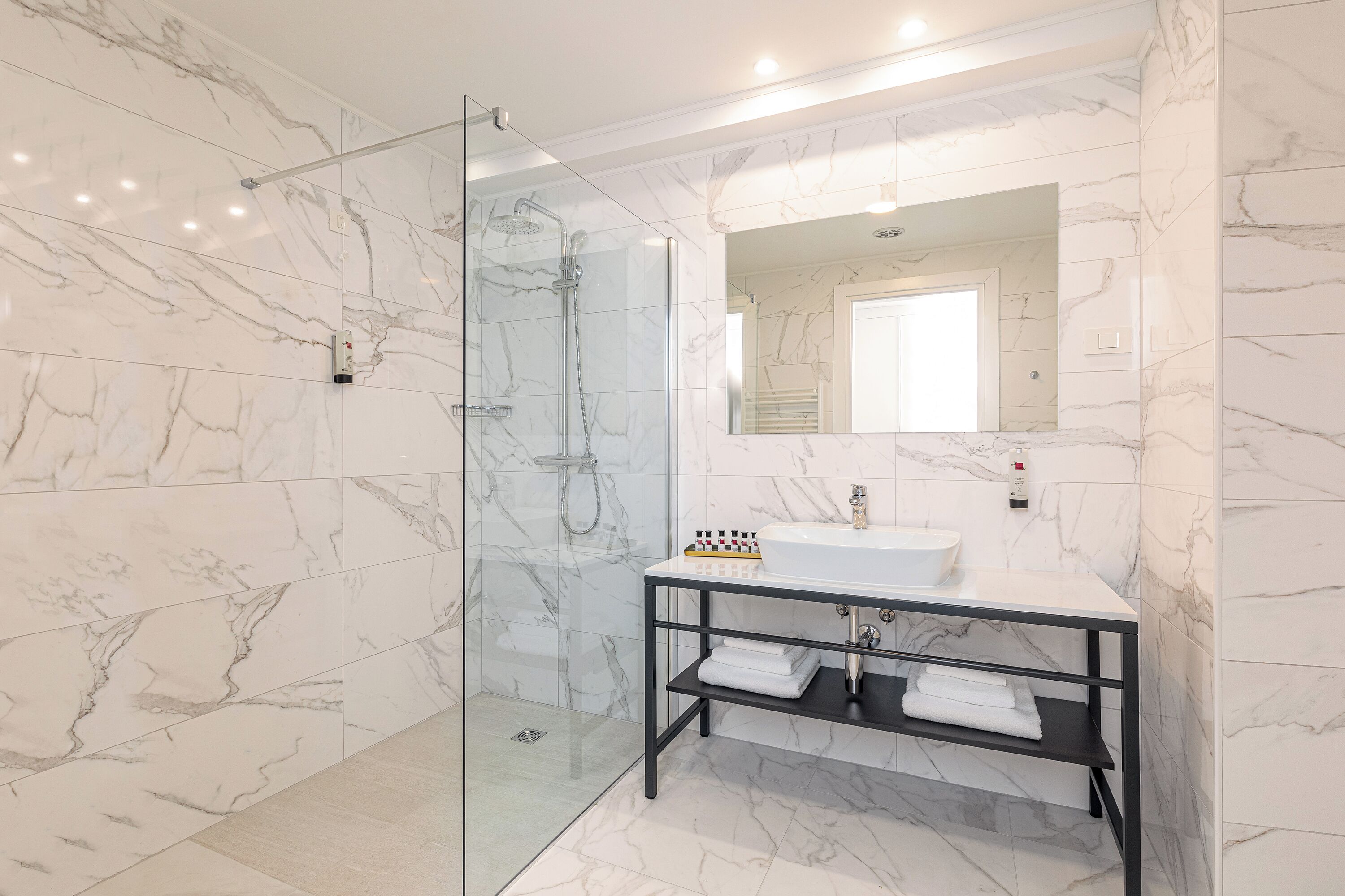 Une salle de bain moderne avec une douche en verre, un lavabo blanc et un sol carrelé en marbre.