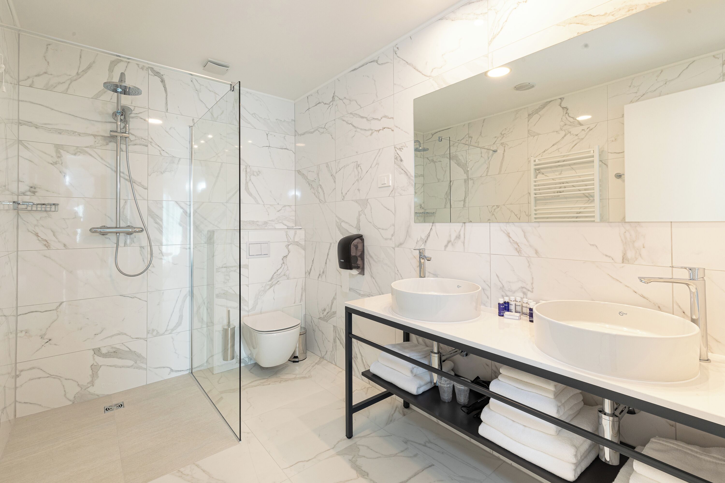 Une salle de bain moderne avec une douche en verre, deux lavabos, un grand miroir et des murs en marbre.