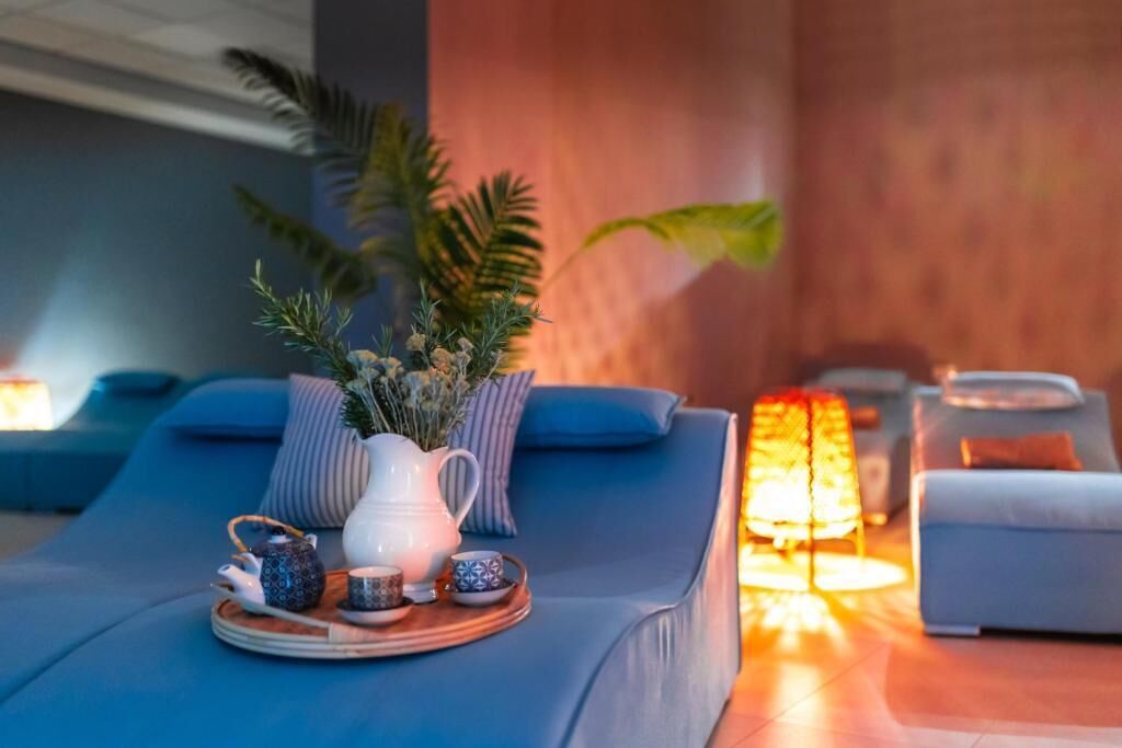 Ein Spa-Raum mit Massageliege, Tablett mit Teekanne und Tassen sowie einer brennenden Kerze.