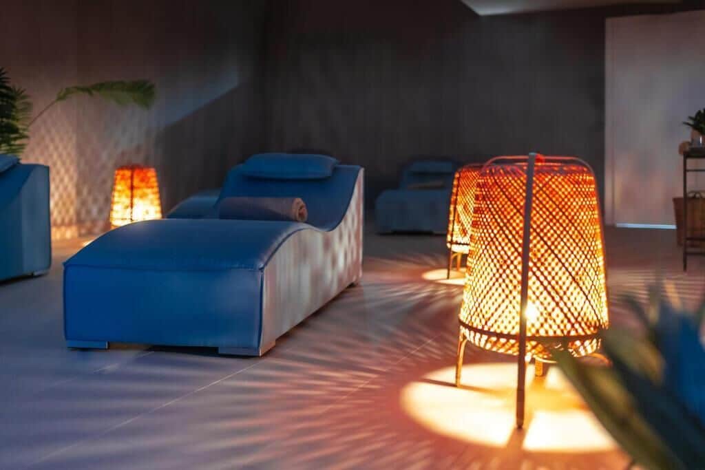 A modern lounge area with a blue sofa, a patterned floor lamp, and a wall-mounted heater.
