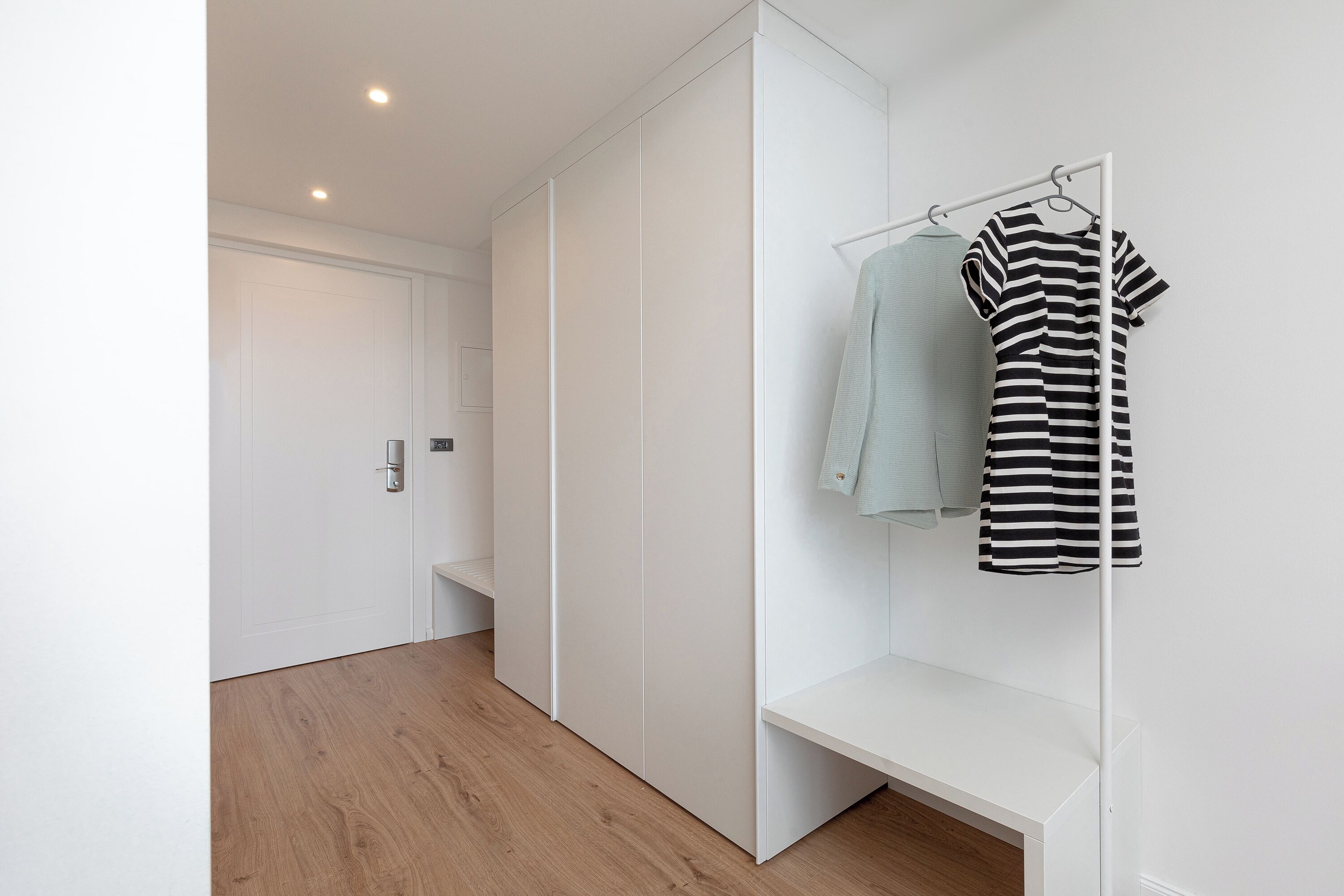 A modern, minimalist hallway with a wooden floor, white walls, and a white bench.